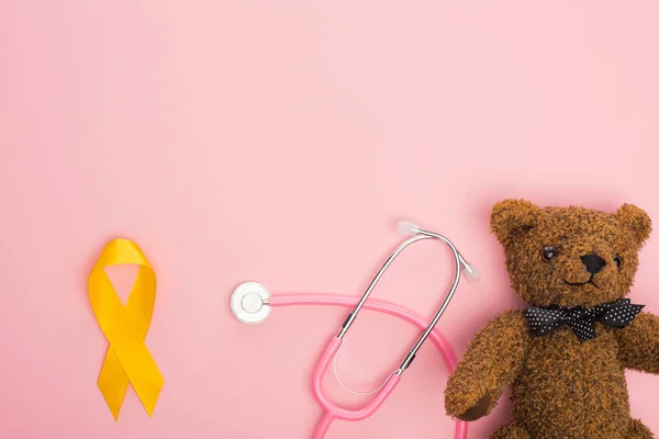 ピンクの背景に黄色のリボンとテディベアのトップビュー 国際小児がんの日の概念 — ストック写真