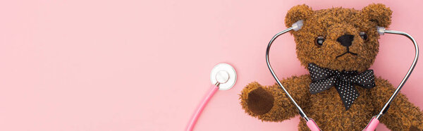 Top view of stethoscope connected with teddy bear on pink background, panoramic shot, international childhood cancer day concept