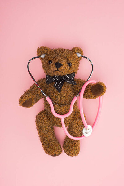 Top view of teddy bear with stethoscope on pink background, international childhood cancer day concept