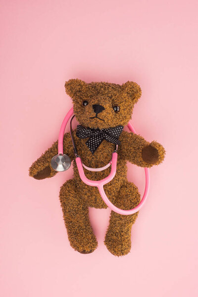 Top view of brown teddy bear with stethoscope on pink, international childhood cancer day concept