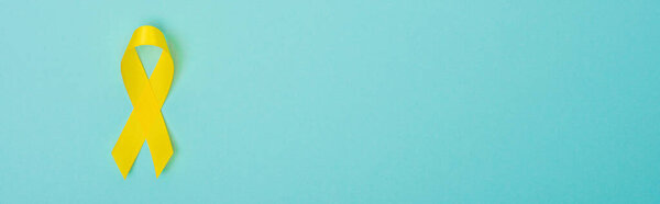 Top view of yellow ribbon on blue background, panoramic shot, international childhood cancer day concept