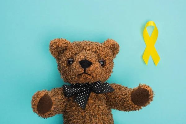 stock image Top view of yellow ribbon next to teddy bear on blue background, international childhood cancer day concept