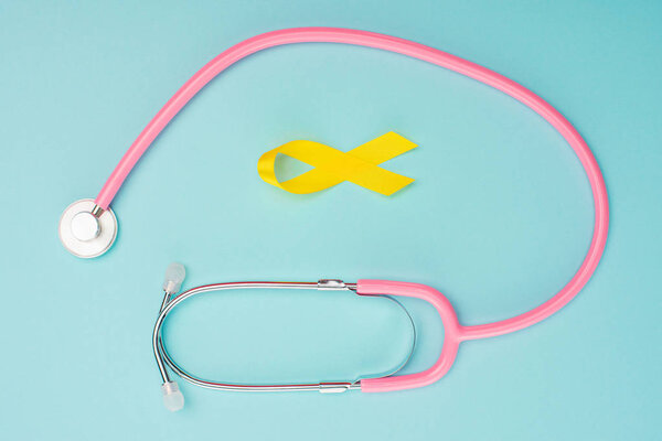 Top view of yellow ribbon and stethoscope on blue background, international childhood cancer day concept