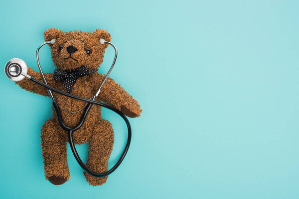 Вид сверху на бурого плюшевого медведя со стетоскопом на синем фоне, концепция Международного дня борьбы с детским раком
