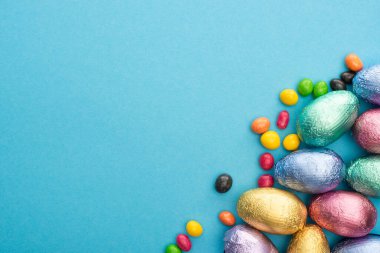 Çikolatalı Paskalya yumurtalarının mavi arka planda renkli tatlılar ile folyo içinde üst görünümü