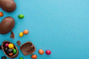 Top view of chocolate Easter eggs with colorful sweets on blue background clipart