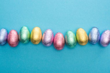 Top view of chocolate Easter eggs in colorful foil on blue background clipart