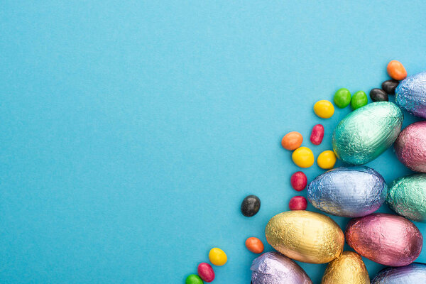 Верхний вид на шоколадные пасхальные яйца в фольге с красочными сладостями на синем фоне
