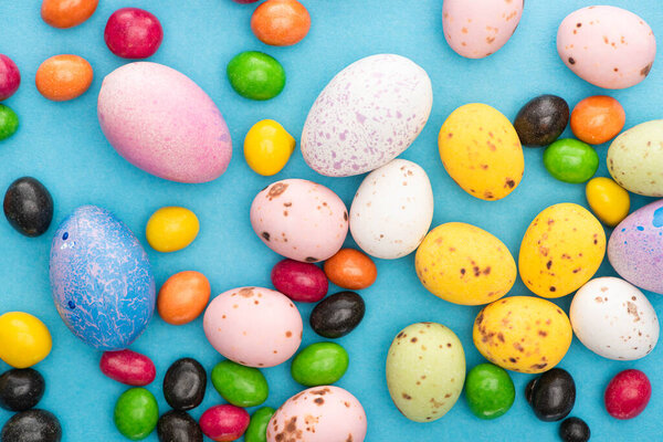 Top view of bright candies, colorful chicken and perail eggs on blue background
