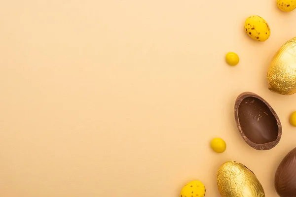 带糖果的巧克力复活节彩蛋和米色背景的黄色鹌鹑彩蛋的顶部视图 — 图库照片
