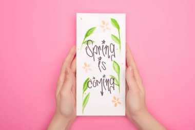 Partial view of woman holding card with spring is coming lettering on pink clipart