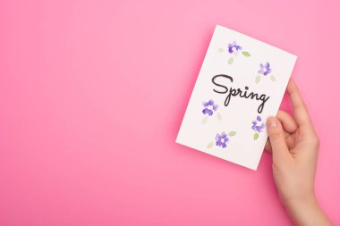 Pembe arka planda bahar harfleri olan kart tutan kadının kısmi görüntüsü
