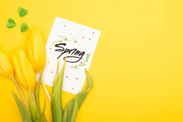 春のレタリング チューリップ 黄色の背景に装飾的な緑の心を持つカードのトップビュー — ストック写真