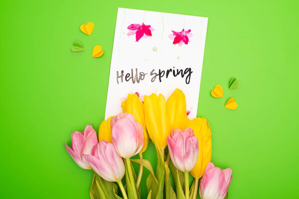 Top view of bouquet, card with hello spring lettering and decorative hearts on pink