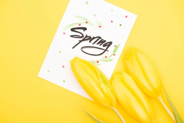 Horní Pohled Kartu Jarním Písmem Tulipány Žlutém Pozadí — Stock fotografie