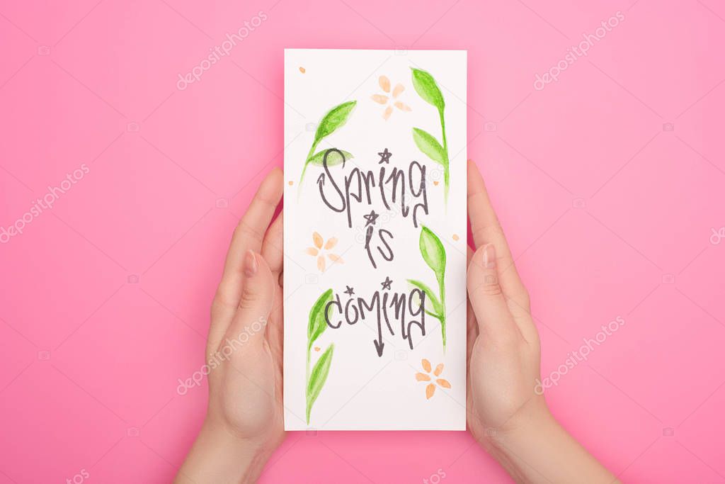 Partial view of woman holding card with spring is coming lettering on pink