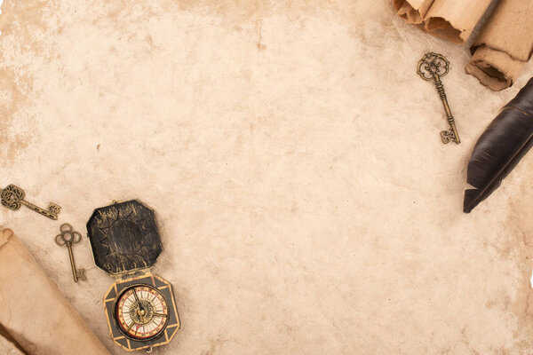 вид сверху на перо, винтажные ключи и компас на старой бумаге
