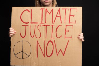 Partial view of blonde woman holding placard with climate justice now lettering isolated on black, global warming concept clipart