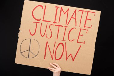 Partial view of woman holding placard with climate justice now lettering isolated on black, global warming concept clipart