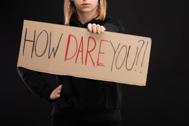 Partial view of woman with outstretched hand holding placard with how dare you lettering isolated on black, global warming concept clipart