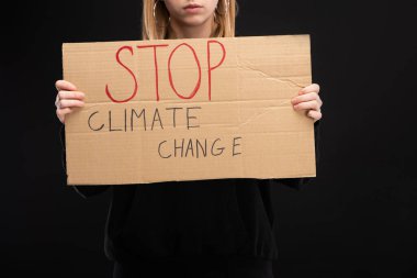 Partial view of blonde woman with placard with stop climate change lettering isolated on black, global warming concept clipart