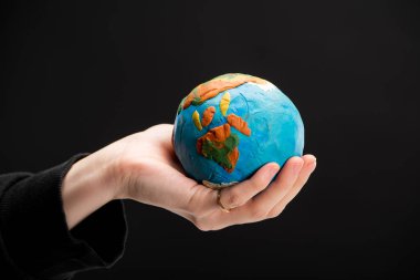 Partial view of plasticine globe in female hand isolated on black, global warming concept clipart