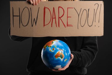Partial view of woman holding globe and placard with how dare you lettering isolated on black, global warming concept clipart