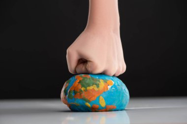 Partial view of woman compressing plasticine globe by fist isolated on black, global warming concept clipart