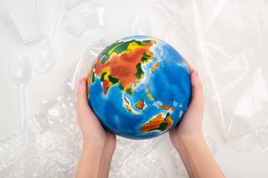 Beyaz arka planda plastik çöpün üzerinde dünyayı tutan bir kadın görüntüsü, küresel ısınma kavramı