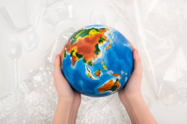 Cropped view of woman holding globe above plastic garbage on white background, global warming concept clipart