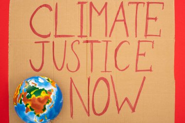 Top view of globe and placard with climate justice now lettering on red background, global warming concept clipart