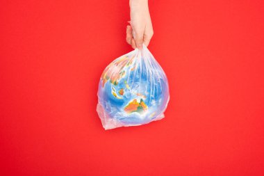 Küresel ısınma kavramının kırmızı arka planda izole edilmiş plastik torba içinde dünyayı tutan kadın görüntüsü
