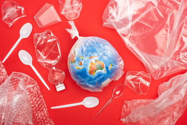 Top view of globe in plastic bag with garbage around isolated on red, global warming concept