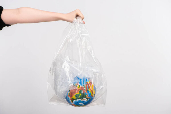 Partial view of woman with outstretched hand holding globe in plastic bag isolated on white, global warming concept