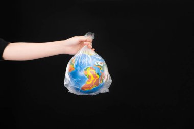 Cropped view of woman holding plastic bag with globe isolated on black, global warming concept clipart