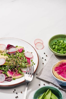 Taze turp salatası, yeşil sebzeler ve beyaz tabaktaki avokado, içinde çatal ve kaselerdeki malzemeler var.