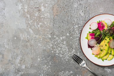 Gri beton yüzeyde çatallı taze turp salatası ve avokado.