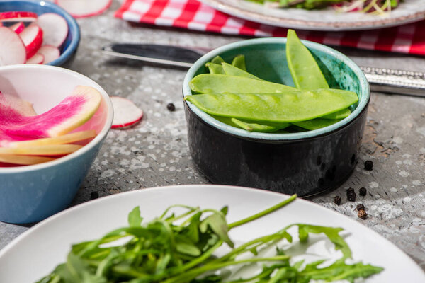 selective focus of fresh radish salad ingredients in bowls on grey concrete surface