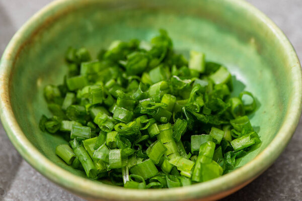 close up view of fresh cut green onion in bowl on grey concrete surface