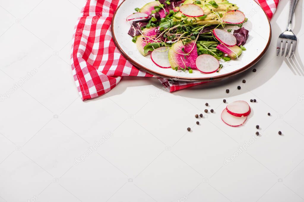 fresh radish salad with greens and avocado on plate on white surface with napkin and fork