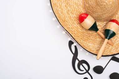 Kağıt yakınındaki sombrero ve marakaların üst görünümü beyaz arkaplandaki müzik notalarını keser