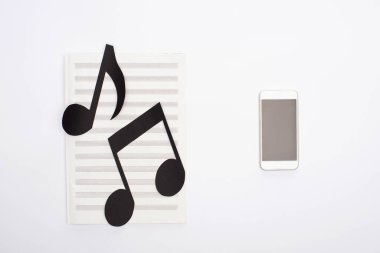 Kağıt kesme notalarının üst görünümü beyaz arkaplanda akıllı telefonun yanındaki müzik kitabında