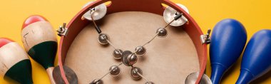 Close up view of tambourine near colorful and blue maracas on yellow background, panoramic shot clipart