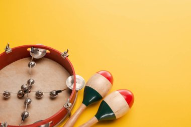 Tambourine near colorful wooden maracas on yellow background clipart