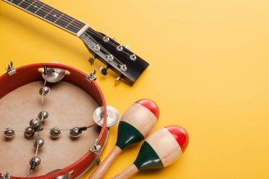 Tambourine near colorful wooden maracas and acoustic guitar on yellow background clipart