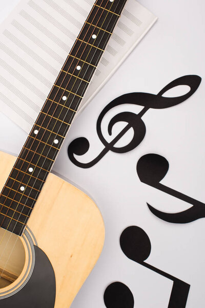 Top view of paper cut notes near music book with acoustic guitar on white background