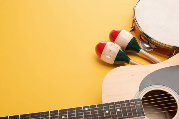 Wooden colorful maracas with tambourine and acoustic guitar on yellow background
