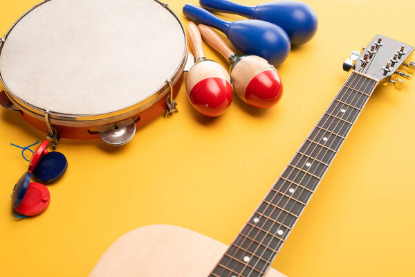 Wooden colorful and blue maracas, tambourine, castanets and acoustic guitar on yellow background