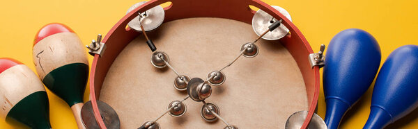 Close up view of tambourine near colorful and blue maracas on yellow background, panoramic shot