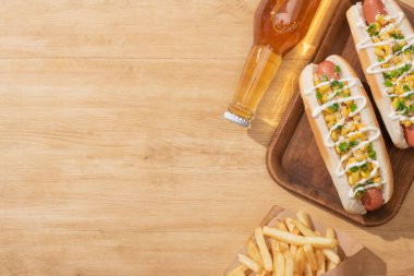 top view of delicious hot dogs with corn, green onion and mayonnaise near french fries and beer on wooden table clipart